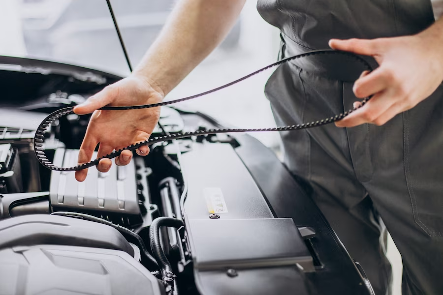 A person holding a serpentine belt in front of an open car hood